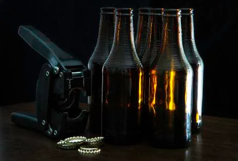 Hand capper with five dark brown bottles and caps and over black background 写真素材