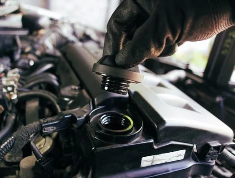 The hand of a car mechanic opens the engine oil cap to inspect Stock Photos