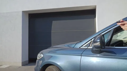 Hand from car window presses remote button in front of residential garage door Stock Footage 333282758