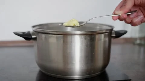 A hand carefully adding butter to a pot, significantly enhancing the flavor and Stock Footage 312327258