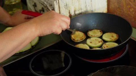 Hand carefully adds a slice of green zucchini to a heated frying pan, while a Stock Footage 281590959