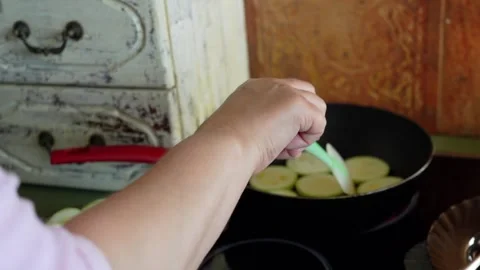 Hand carefully adds a slice of green zucchini to a heated frying pan, while a Stock Footage 282082598