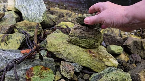 Hand carefully balancing a stone while building a stone tower Stock Footage 344058651