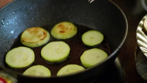Hand carefully flips a zucchini slice in a hot pan, while others brown and Stock Footage 280916310