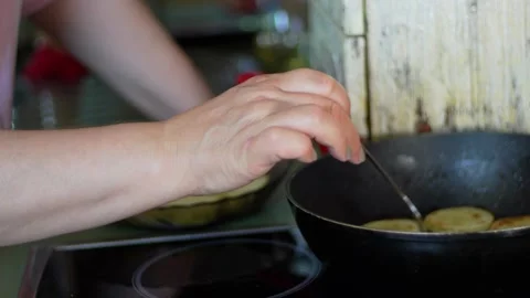 Hand carefully flips a zucchini slice in a hot pan, while others brown and Stock Footage 281590920