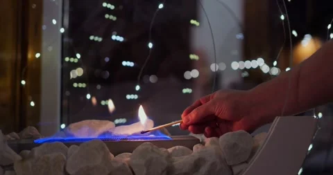 Hand carefully lights biofire with match, bringing biofire soft blue flames to Stock Footage 289730027