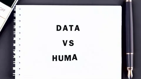 A hand carefully writes DATA VS HUMAN on a small white spiral notebook placed on Stock Footage 335094196