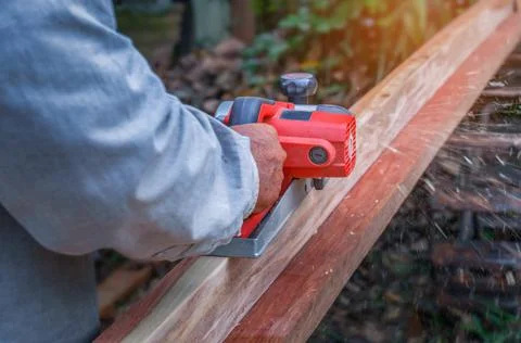 Hand of carpenter using electric planer with wooden plank in carpentry workshop Stock-Fotos