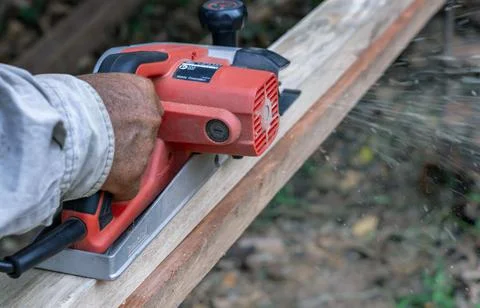 Hand of carpenter using electric planer with wooden plank in carpentry workshop Stock-Fotos