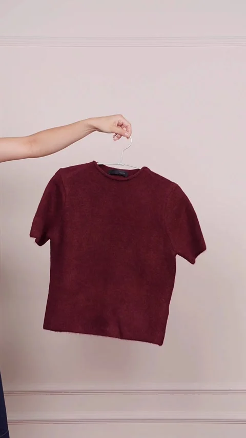 Hand catching folded maroon tshirt on metal clothes hanger Video stock 331774017