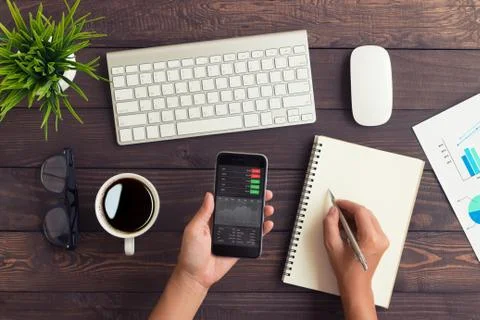 Hand checking stock graph on phone and write note Stock Photos