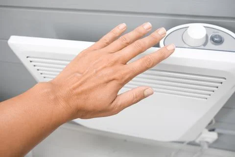 A hand checking temperature of heating convector on the wall, air heating the Stock Photos