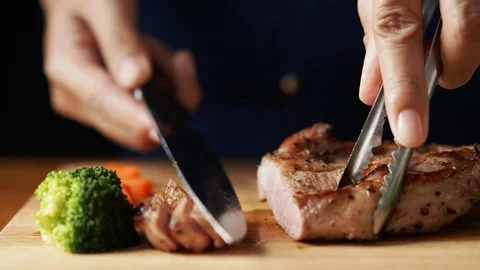 Hand of chef cut a steak with knife into pieces on  brown wooden board Stock Footage 120215675