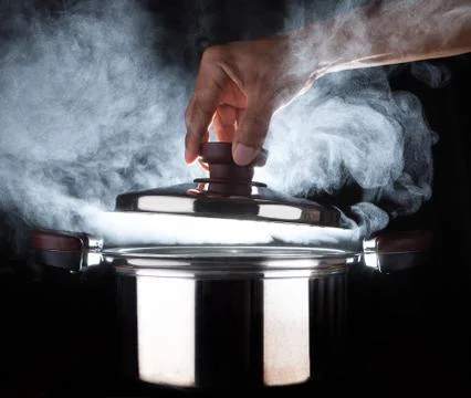 Hand of chef open hot stream pot with beautiful studio lighting against black Stock-Fotos