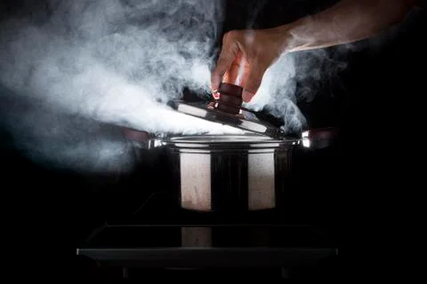 Hand of chef open hot stream pot with beautiful studio lighting against black 写真素材