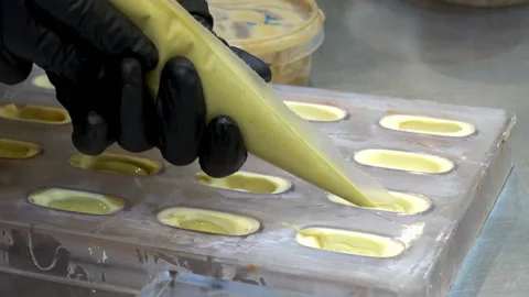 The hand of chef pours white chocolate into plastic molds Video stock 101871140