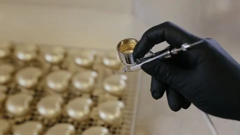 Hand of chef using airbrush for cake decorating. Lots of gold colored heart Stock Footage 134345411