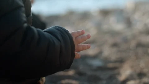 Hand of a child in a black jacket playing with pebbles on the seashore Stock Footage 127061989