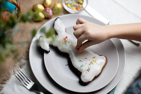 Hand of child decorating baked Easter bunny gingerbread cookie with multi Stock Photos