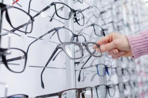 Hand choosing eyeglass frames from display wall in optical store closeup 写真素材
