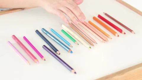 Hand choosing three colored pencils from rainbow gradient on white table Stock Footage 331719115