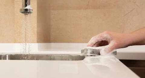 Hand with a cleaning sponge washes the surface of the kitchen with foam Stock Photos