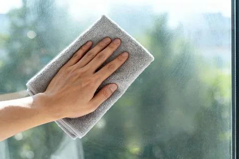 Hand cleaning a window with a microfiber cloth on a sunny day Stock Photos