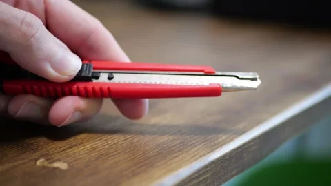 Hand clicking red mini stationery knife wooden desk surface sharp plastic snap Stock Footage 320894764