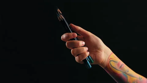 A hand in close-up on a black background holds pencils Stock Footage 184039790