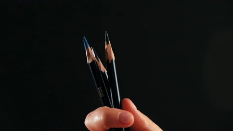 A hand in close-up on a black background holds pencils Video stock 184041637
