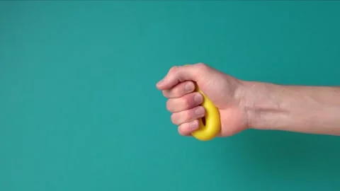 Hand close-up squeezes yellow hand expander many times against blue background Stock Footage 145457698