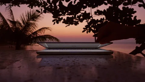 Hand Closing Laptop With Blank Screen On Table Against Tropical Sunset With Palm Stock Footage 332305318
