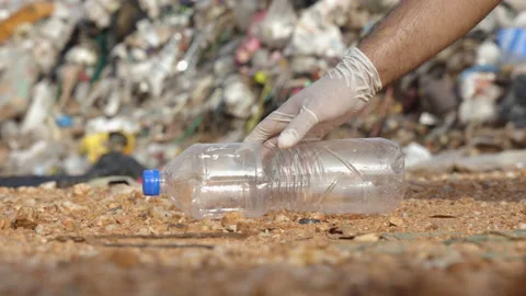 Hand collecting a plastic bottle in front of a large mountain and a pile of tras Stock Footage 158883148