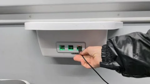 Hand connecting charging cable to USB outlet inside train interior. Video stock 328639146
