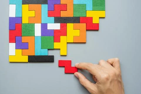 Hand connecting geometric shape block with colorful wood puzzle pieces. logic Stock Photos