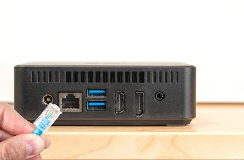 Hand connecting a network cable to back panel of micro computer showing conne Stock Photos