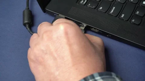 Hand connects USB-C cable to laptop port while other cables and USB devices are Stock Footage 329430824