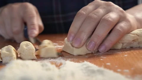Hand of cook with knife cuts off pieces of dough on table sprinkled with flour Video stock 241284853