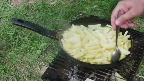 The hand of the cook stirs the potatoes with a spoon in a pan on the grill, 스톡 동영상 217519293