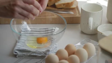 Hand cracking eggs into glass bowl on kitchen counter Stock Footage 337957664