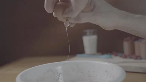 Hand cracking eggs into a white bowl of flour for baking a cake Stock Footage 346107375