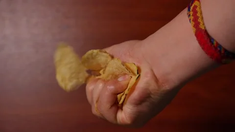 Hand crushing potato chips, showing texture and pressure on a wooden background. Stock Footage 308674244