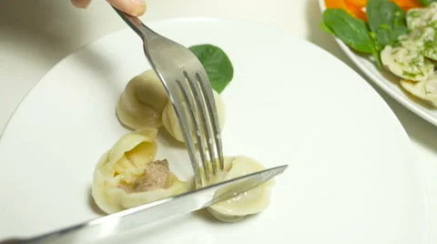 Hand cuts pelmeni in a half on white plate with fork and knife Stock Footage 63780931