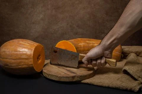 The hand cuts the pumpkin in half with an ax. Long pumpkin. Stock Photos