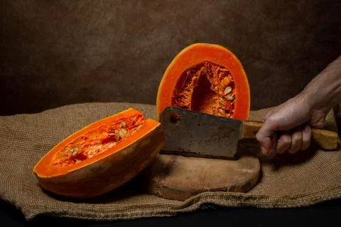 The hand cuts the pumpkin in half with an ax. Stock Photos