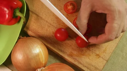 Hand cuts red cherry tomatoes in half on wooden board, revealing juicy texture Stock Footage 318603041