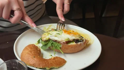 Hand cutting breakfast sandwich, a fried egg, avocado, green arugula, and bagel, Video stock 332834718