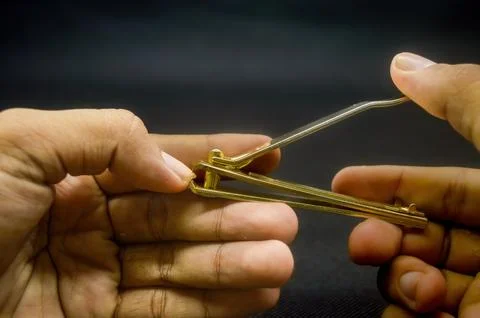 Hand cutting nails using a gold nail clipper isolated on black background Stock Photos