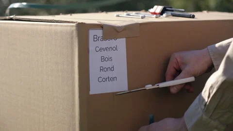 Hand cutting open a sealed cardboard box with a cutter during outdoor unpacking Stock Footage 327721516