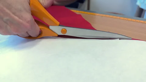 Hand cutting red fabric with scissors on wooden table, crafting process visible Vídeos de archivo 346491796